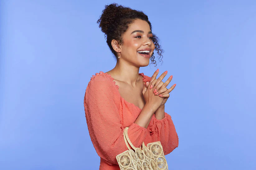 Mujer sonriendo de pie, con las manos cruzadas y las uñas postizas de color coral