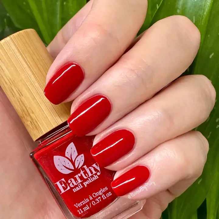 Mano de mujer con las uñas rojas sujetando el frasco del esmalte de uñas sin tóxicos Rojo Pasión de Mother Nailture