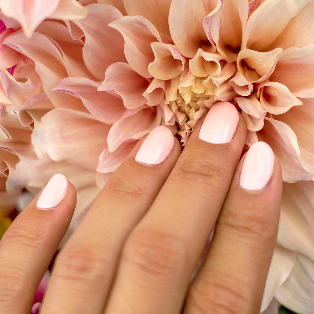 Mano de mujer con las uñas rosas naturales y brillantes del esmalte de uñas sin tóxicos de Nailtural tocando una flor