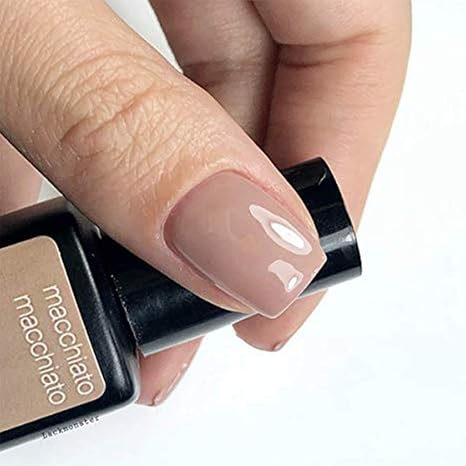 Mano con uñas beige Macchiato sujetando frasco de esmalte de gel para uñas semipermanentes