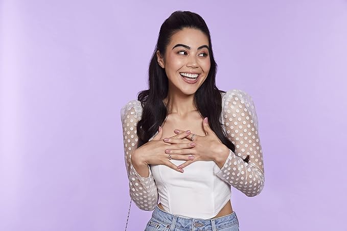 Mujer sonriendo de pie, con las manos cruzadas y las uñas postizas rosas.