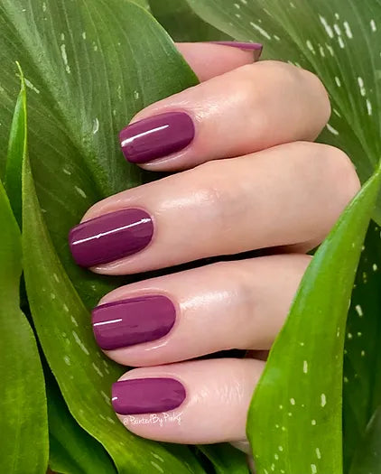 Mano de mujer con las uñas moradas púrpura ciruela naturales y brillantes del esmalte de uñas sin tóxicos de Mother Nailture