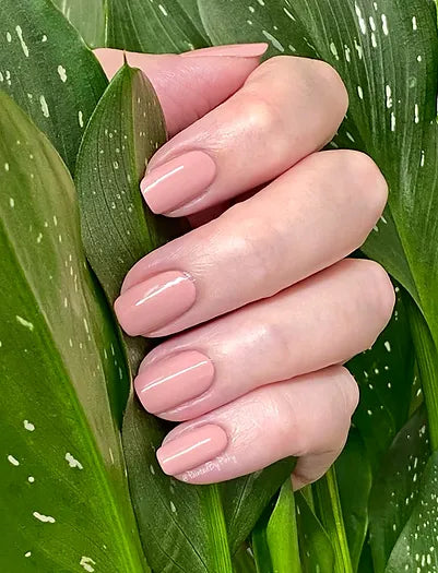 Mano de mujer con las uñas rosas Jazmín, naturales y brillantes del esmalte de uñas sin tóxicos de Mother Nailture