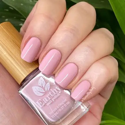 Mano de mujer con las uñas rosas sujetando el frasco del esmalte de uñas sin tóxicos rosa Flor de Cerezo