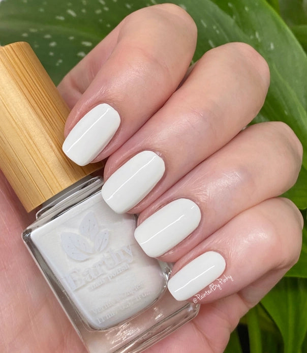 Mano de mujer con las uñas blancas sujetando el frasco del esmalte de uñas sin tóxicos Rosa Blanca de Mother Nailture