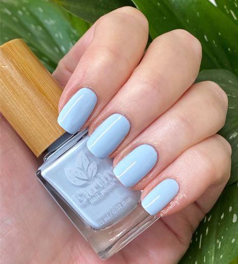 Mano de mujer con las uñas azules sujetando el frasco del esmalte de uñas sin tóxicos Azul Islandia de Mother Nailture