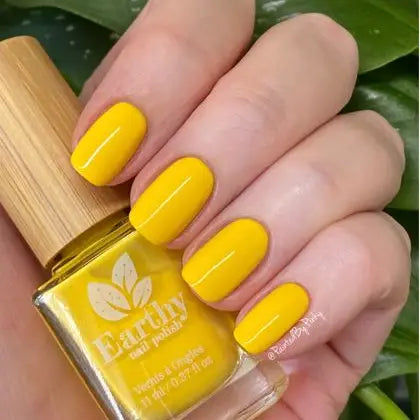 Mano de mujer con las uñas amarillas sujetando el frasco del esmalte de uñas sin tóxicos Buttercup de Mother Nailture