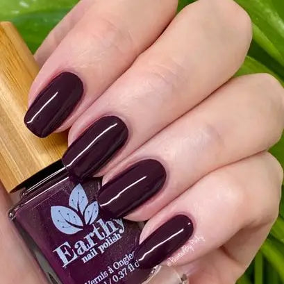 Mano de mujer con las uñas púrpura sujetando el frasco del esmalte de uñas sin tóxicos Purple Rain de Mother Nailture