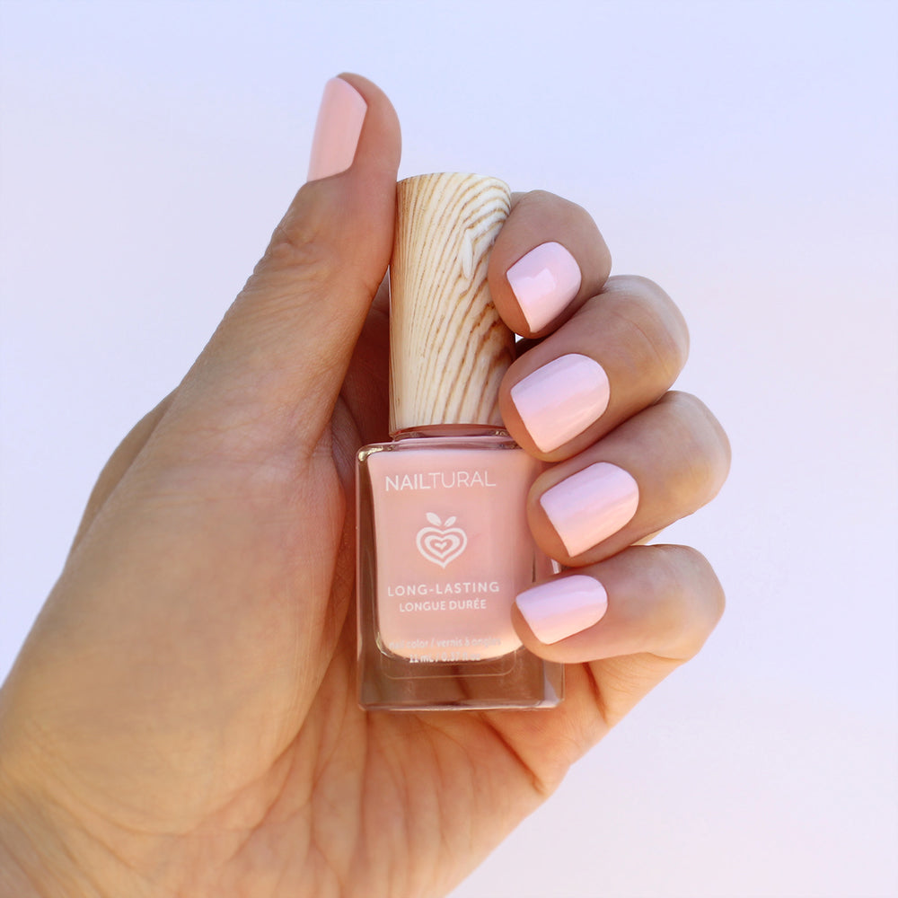 Mano de mujer con las uñas rosas sujetando el frasco del esmalte de uñas sin tóxicos de Nailtural